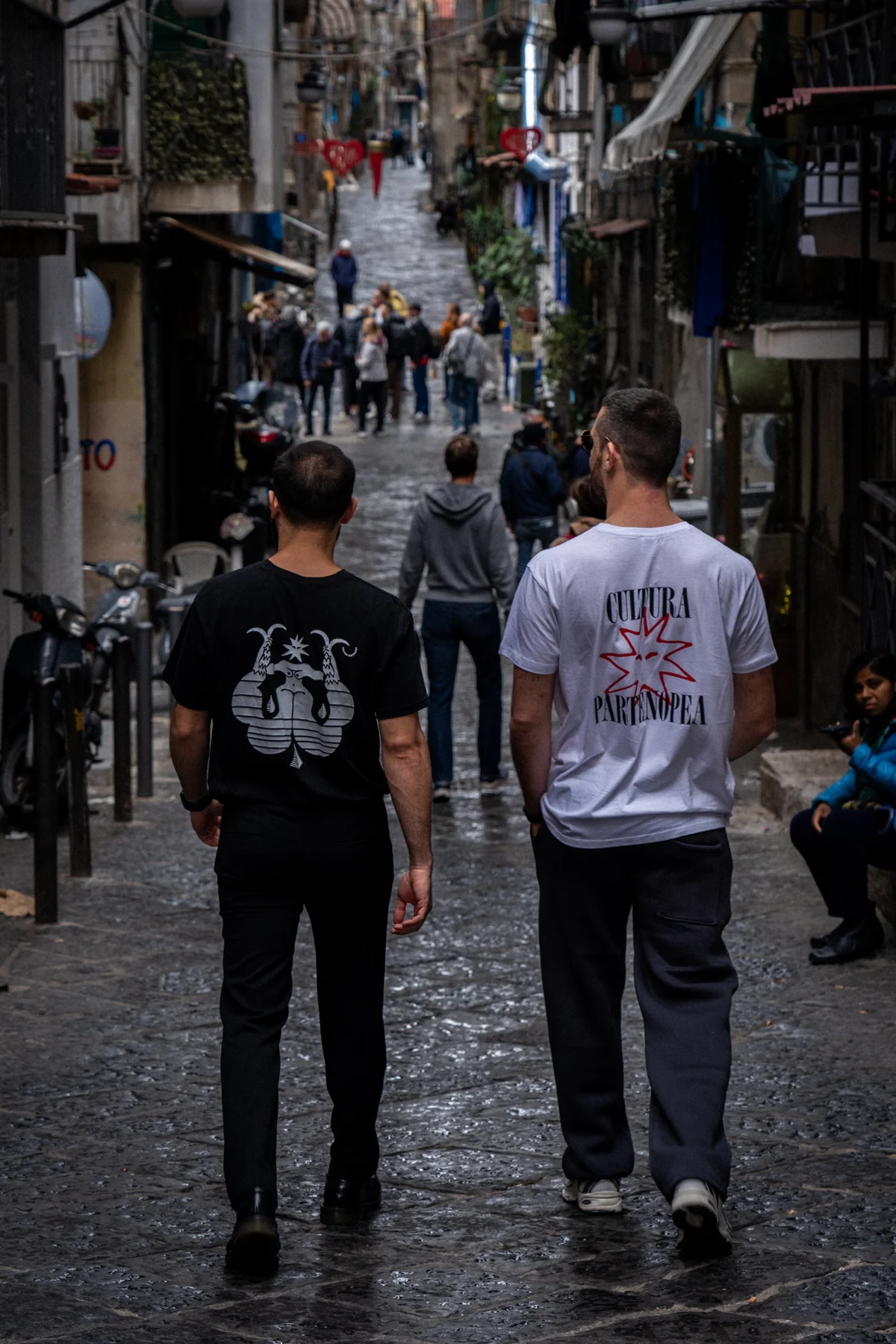 Due persone indossano le magliette Cultura Partenopea per le strade di Napoli.